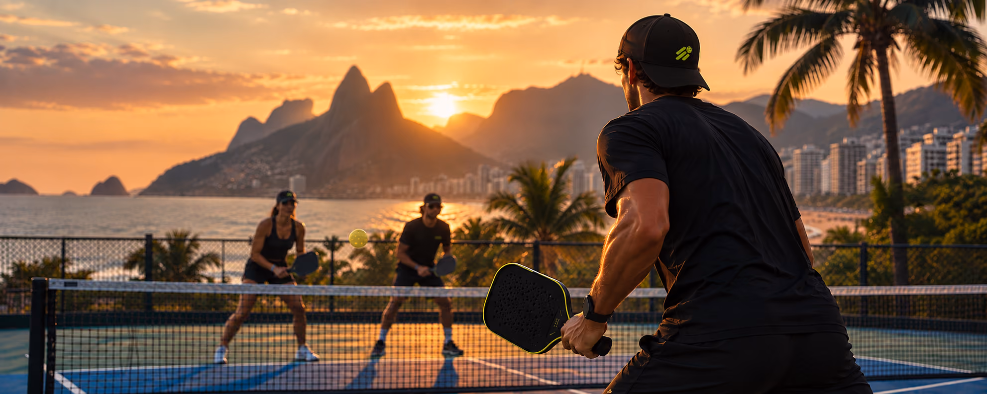 Partida de pickleball ao entardecer no Rio de Janeiro, com o logo DINK no boné do jogador em primeiro plano.